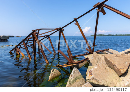 A weathered rusted metal structure extends into blue coastal waters 133490117