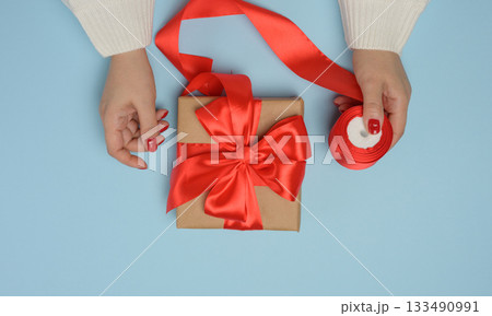 Two female hands holding gift boxes tied with a red ribbon on a blue background 133490991
