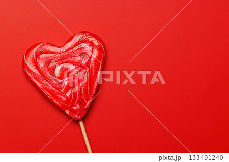 Heart-shaped lollipop on a vibrant red background 133491240