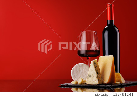 A refined selection of aged cheeses presented on a board, accompanied by a glass of wine 133491241
