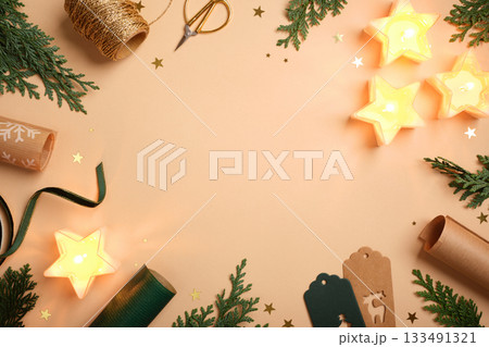 Christmas frame with star candles, fir branches, gift tags, and wrapping supplies on beige background. Copy space for text or design. 133491321