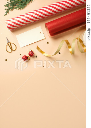 Christmas gift wrapping with red and white striped wrapping paper, ribbon, baubles, scissors, cedar spruce on beige backdrop. Copy space. 133491322