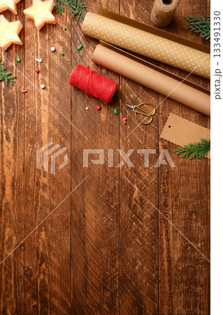 Christmas wrapping background with paper rolls, rope, gift tags and scissors on dark wooden desk. Copy space for text. 133491330