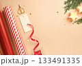 Christmas gift wrapping with red and white striped wrapping paper, ribbon, scissors, thuja spruce, candles on beige backdrop. Copy space. 133491335