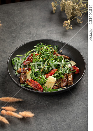 Fresh arugula salad with beef and sundried tomatoes 133491814