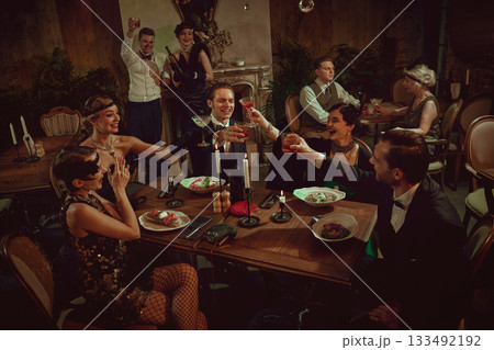 Stylish retro friends celebrating and toasting at festive dinner table setting 133492192