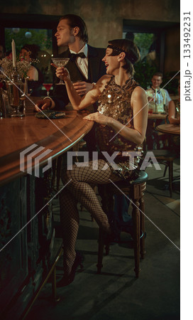 Laughing young woman in sparkling retro dress enjoying cocktails at vintage bar Laughing young woman in sparkling retro dress enjoying cocktails at vintage bar 133492231