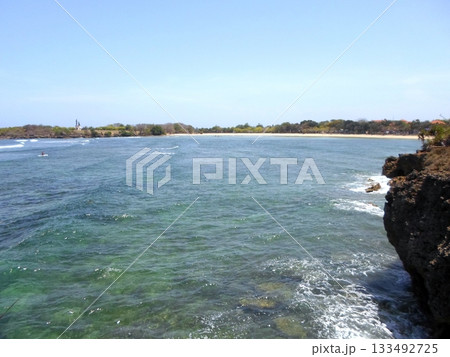 Rocky Cliff Overlooking a Sandy Beach with Surfers Riding Waves on a Clear Day Rocky Cliff Overlooking a Sandy Beach with Surfers Riding Waves on a Clear Day 133492725