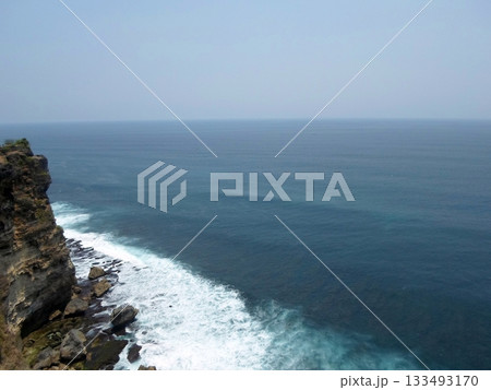 A Cliffside View of the Ocean with Waves Crashing Against Rocks Under a Clear Blue Sky 133493170
