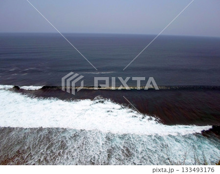 Ocean Waves Crashing Against a Cliffside with a Vast View of the Sea Under a Clear Sky 133493176
