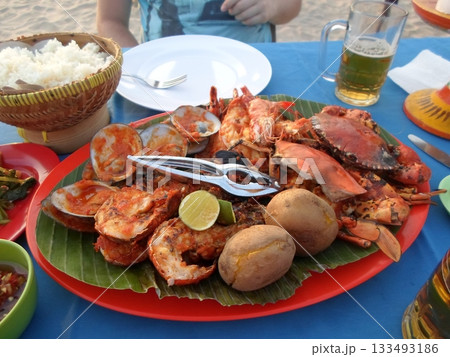 A Beachside Seafood Feast with Grilled Lobster, Crab, and Clams on a Red Platter with Rice and Beer A Beachside Seafood Feast with Grilled Lobster, Crab, and Clams on a Red Platter with Rice and Beer 133493186