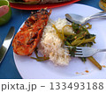 A Plate of Grilled Lobster with Rice and Sauteed Vegetables on a Beachside Table with Utensils 133493188