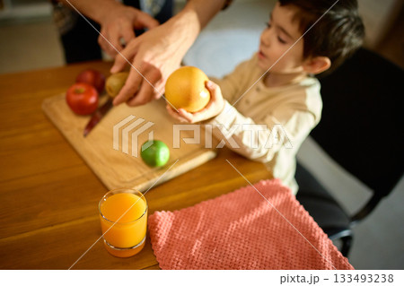 Bright orange juice in glass beside fruits during warm joyful father and son moment Bright orange juice in glass beside fruits during warm joyful father and son moment 133493238