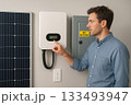 Man Checking Solar Energy System Display with Solar Panel and Net Metering Box on Wall 133493947