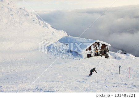 A snowboarder rides down a snowy slope above dark clouds in a valley A snowboarder rides down a snowy slope above dark clouds in a valley 133495221