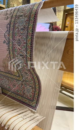Carpet weaving loom with intricate design and threads in background 133496439