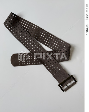 Brown leather belt with perforated design on white surface, suitable as fashion accessory background 133496456
