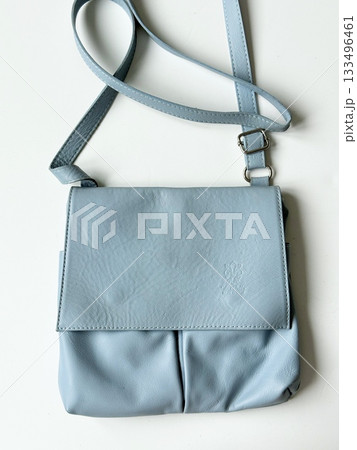 Light blue leather crossbody bag on white table, with adjustable strap and embossed logo 133496461
