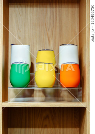 Colorful cups arranged neatly on a wooden shelf in a bright space 133496750