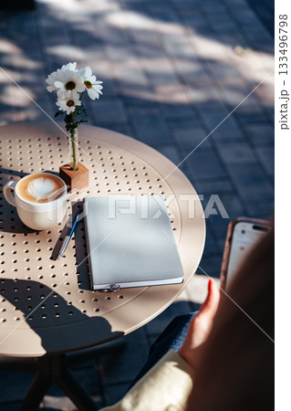 Cozy coffee table with latte, notebook and flowers in a sunny outdoor setting Cozy coffee table with latte, notebook and flowers in a sunny outdoor setting 133496798