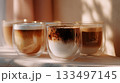 Four coffee drinks in glass cups with layers sitting on a counter in warm sunlight 133497145