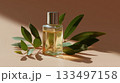 Glass bottle of perfume placed on a neutral background with leaves nearby 133497158