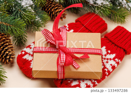 Gift box on winter mittens, snowy fir branches and beige background Gift box on winter mittens, snowy fir branches and beige background 133497286