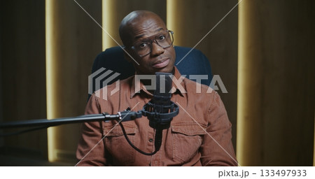 Charismatic Male Host With Glasses Smiling and Looking Directly at Camera While Recording Podcast 133497933