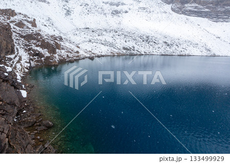 雪の積もった湖畔の岩場と青い水 133499929