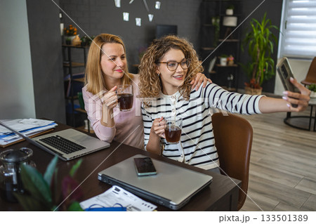 Two female colleagues are taking selfies and drinking coffee 133501389