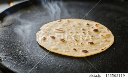 Freshly cooked flatbread on hot griddle with steam rising above 133502119