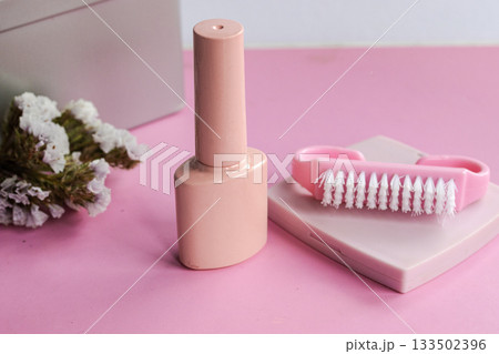 Pink nail polish bottle and a manicure brush with white bristles on a pastel pink background, symbolizing self care, beauty, and wellness treatment for healthy fingernails 133502396