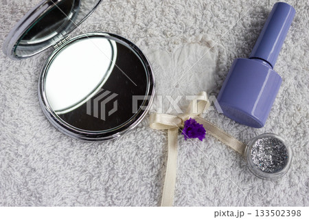Self care essentials artfully arranged on a soft white towel. Featuring a compact mirror. Vibrant nail polish. Shimmering cosmetic glitter. And delicate decorative elements 133502398