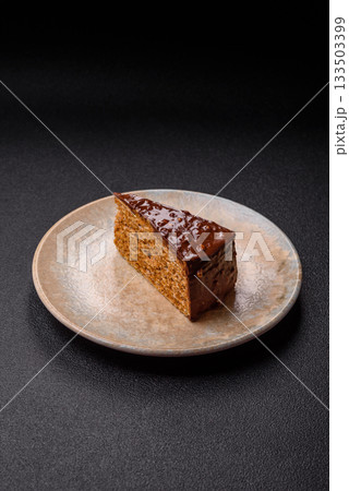 A slice of sweet layered cake covered in chocolate with nuts and caramel. A slice of chocolate cake 133503399