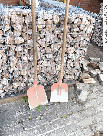 Two shovels leaning against a gabion wall Two shovels leaning against a gabion wall 133503456