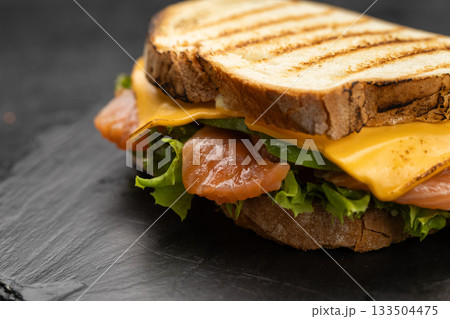 Grilled salmon and cheddar sandwich with lettuce on slate board, lemon and capers 133504475