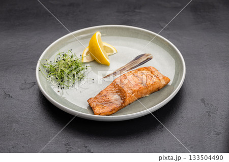 Grilled salmon fillet with lemon and microgreens on plate, gourmet restaurant plating 133504490