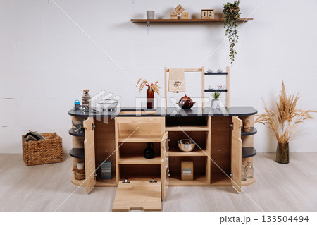 Wooden kids play kitchen with shelves and accessories in minimalist nursery interior 133504494