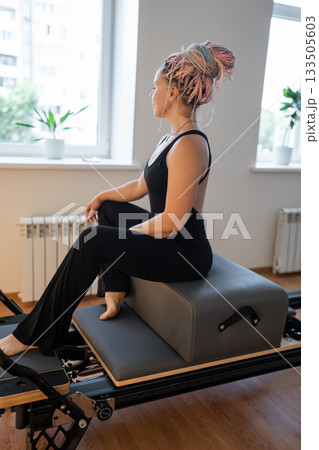 Happy and Tired woman having rest after pilates workout. Tired and exhausted female athlete sitting on reformer bed. Happy and Tired woman having rest after pilates workout. Tired and exhausted female athlete sitting on reformer bed. 133505603