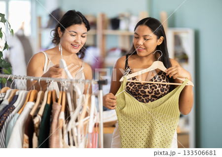 Two young women choosing summer dresses or tops in clothing store Two young women choosing summer dresses or tops in clothing store 133506681