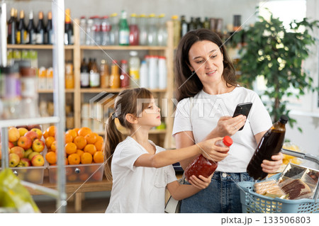 Girl with mother customers at shop scans QR code on juice package using phone camera 133506803