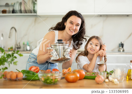 Mother holding saucepan and preteen daughter standing at table Mother holding saucepan and preteen daughter standing at table 133506995