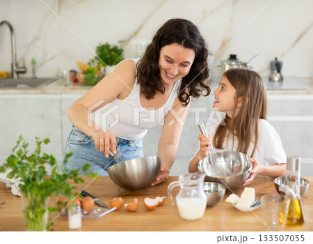 Happy mother and her daughter whisking ingredients in metal bowl in the kitchen Happy mother and her daughter whisking ingredients in metal bowl in the kitchen 133507055