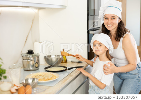 Mom and her daughter in white chief hats fry pancakes Mom and her daughter in white chief hats fry pancakes 133507057