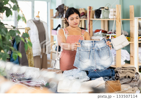 Positive young woman chooses fashionable shorts in clothing store 133507114