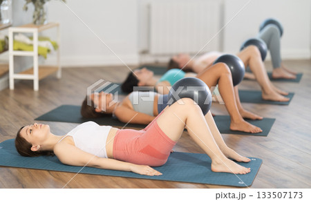 Young girl doing bridge exercise with ball group pilates session Young girl doing bridge exercise with ball group pilates session 133507173