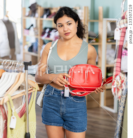 Latina woman choosing a stylish handbag in store with interest Latina woman choosing a stylish handbag in store with interest 133507219