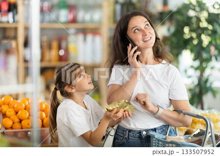 Family buying groceries in supermarket - mother talking on her mobile phone, little daughter asking to buy sweets 133507952