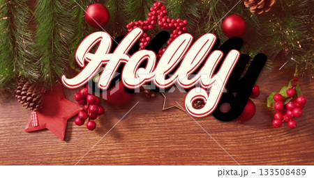 Showcasing decorative sign 'Holly' on wooden tabletop, with evergreen branches, red berries, cones Showcasing decorative sign 'Holly' on wooden tabletop, with evergreen branches, red berries, cones 133508489