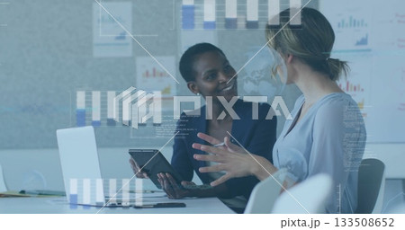 Reviewing two colleagues in business attire analyzing charts on tablet and laptop at office table Reviewing two colleagues in business attire analyzing charts on tablet and laptop at office table 133508652